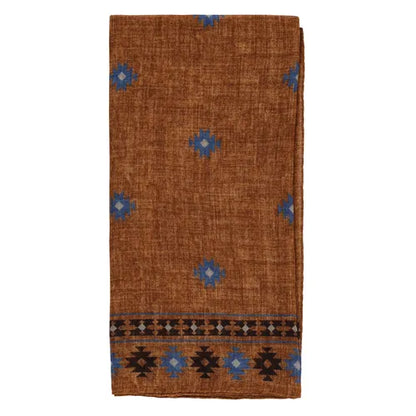 A folded brown wool bandana from Amanda Christensen features an Inca-inspired blue geometric print and a striking black and blue patterned border along one edge. The woven texture and elegant, simple design make it versatile as a scarf, shawl, or decorative accessory. , available at Richard Gelding Mayfair