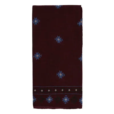 A folded maroon Amanda Christensen wool bandana, featuring an Inca pattern with a border of blue geometric motifs and small white diamonds; similar blue designs are sparsely scattered across the minimal and symmetrical cloth. , available at Richard Gelding Mayfair