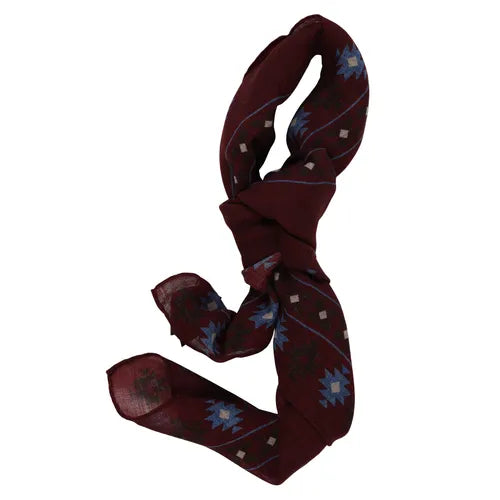A wool bandana from Amanda Christensen featuring an Inca-inspired print in blue and white, tied in a loose knot. The fabric is lightweight and semi-sheer, with the geometric patterns evenly distributed across the bandana. , available at Richard Gelding Mayfair