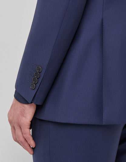 A close-up shows a person’s left arm and hand in a Canali Blue Wool Twill Single Breasted Suit. The dark blue jacket has four black sleeve buttons, with crisp tailoring and smooth fabric, set against a plain light background. , available at Richard Gelding Mayfair