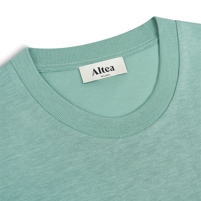Close-up of a green Lyocell crew-neck T-shirt by Altea, with a ribbed collar and white brand label sewn inside the neckline. The shirt is laid flat on a white background. , available at Richard Gelding Mayfair
