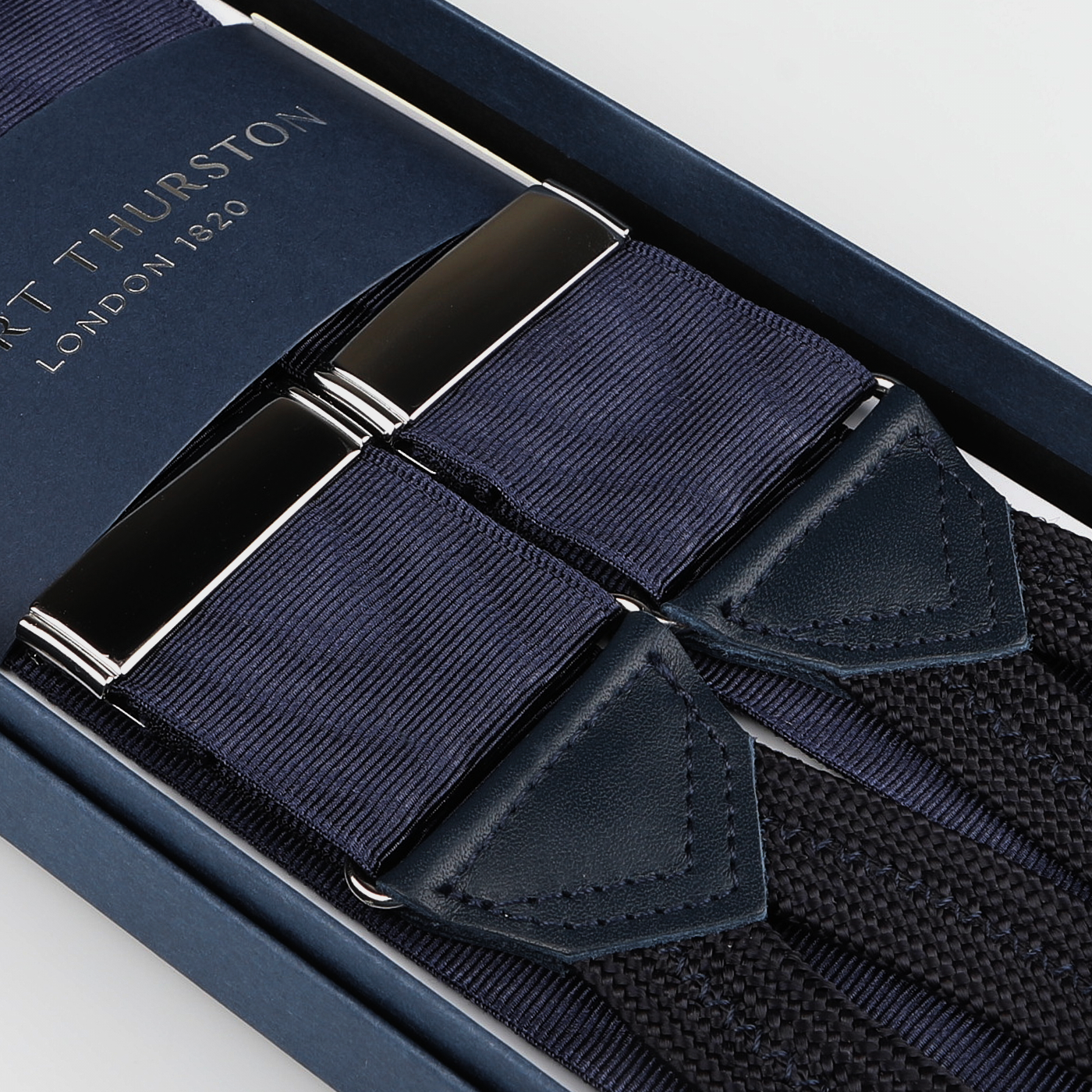 A close-up of Albert Thurston Navy James Bond Moiré 38 mm Braces with leather accents and silver clasps, elegantly boxed and inspired by the iconic suspenders seen in Casino Royale.