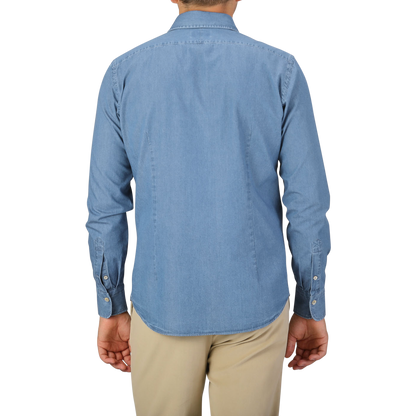 A person is standing with their back facing the camera, wearing an Alessandro Gherardi Light Blue Cotton Denim Single Cuff Shirt and beige pants.