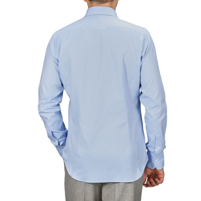 A person wearing an Alessandro Gherardi Light Blue Cotton Oxford Single Cuff Shirt and gray pants, facing away from the camera with one hand in their pocket.