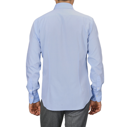 A person wearing a light blue Sky Blue Cotton Twill Single Cuff Shirt by Alessandro Gherardi and gray pants, viewed from the back.