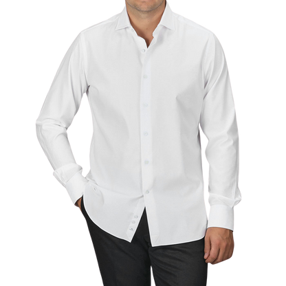 A man wearing an Alessandro Gherardi White Cotton Twill Single Cuff Shirt and black pants stands with his hands in his pockets against a plain gray background.