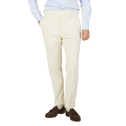 The man is dressed in a white suit, consisting of formal Cream White Cotton Twill Updated Gurkha Trousers and a slim-cut blue shirt from Alexander Kraft Monte Carlo.