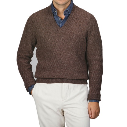 A person wearing an Altea Brown Wool Chevron Knit V-Neck over a blue denim shirt, paired with light beige pants.