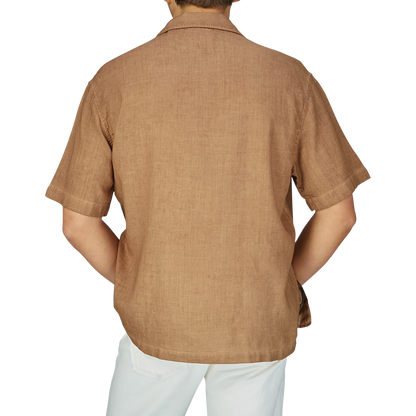Man wearing an Altea Tobacco Brown Linen Blend Camp Collar Shirt with mother-of-pearl buttons and white pants, viewed from the back.