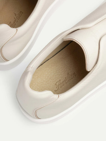 Close-up of the Ivory Grain Leather Slip-On Sneaker by Aurélien. Crafted from light beige grain leather with textured insoles and visible stitching, these laceless sneakers feature a minimalist design against a plain background. , available at Richard Gelding Mayfair