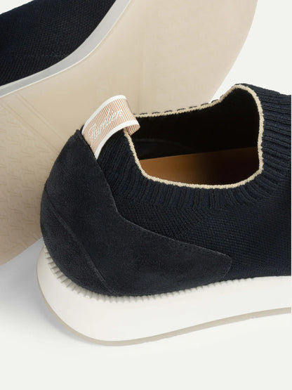 Close-up of the heel of Aurélien Navy Active Knit Wool Sneakers featuring a knit upper, suede overlay, white rubber sole, and beige pull tab with white script text. The light, neutral background highlights their effortless casual luxury. , available at Richard Gelding Mayfair