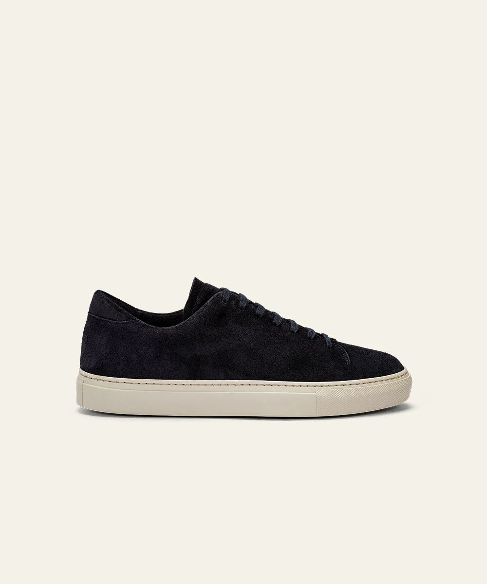 The Azaleri Midnight Blue Suede Sneakers Cannaregio are shown in side profile with matching navy laces, a clean minimalist design, and a light beige rubber sole, set against an off-white background. No logos or patterns are visible. , available at Richard Gelding Mayfair