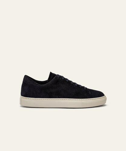 The Azaleri Midnight Blue Suede Sneakers Cannaregio are shown in side profile with matching navy laces, a clean minimalist design, and a light beige rubber sole, set against an off-white background. No logos or patterns are visible. , available at Richard Gelding Mayfair