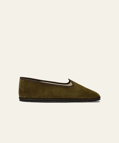 The Azaleri Olive Green Suede Friulane Certosa slipper features a low profile, slightly pointed toe, dark brown trim, and black textured sole. Displayed from the side on a plain beige background. , available at Richard Gelding Mayfair