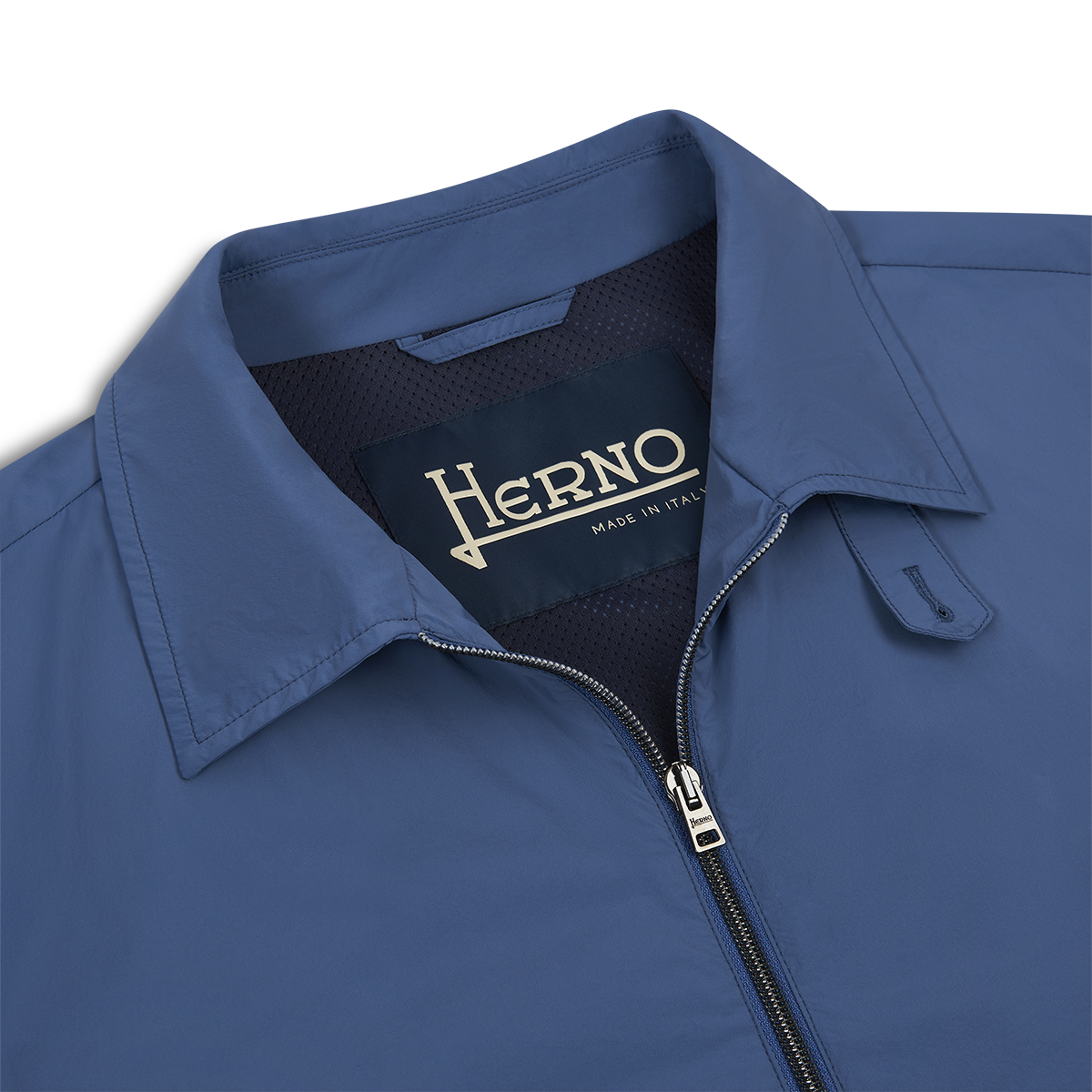 Close-up of the Herno Blue Lightweight Nylon Zip Jacket, showing a visible collar, zipper, and a dark inner label reading “Herno Made in Italy” in cream text. The smooth nylon fabric stands out against a white background. , available at Richard Gelding Mayfair