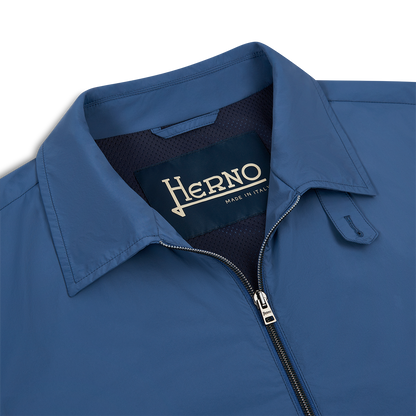 Close-up of the Herno Blue Lightweight Nylon Zip Jacket, showing a visible collar, zipper, and a dark inner label reading “Herno Made in Italy” in cream text. The smooth nylon fabric stands out against a white background. , available at Richard Gelding Mayfair