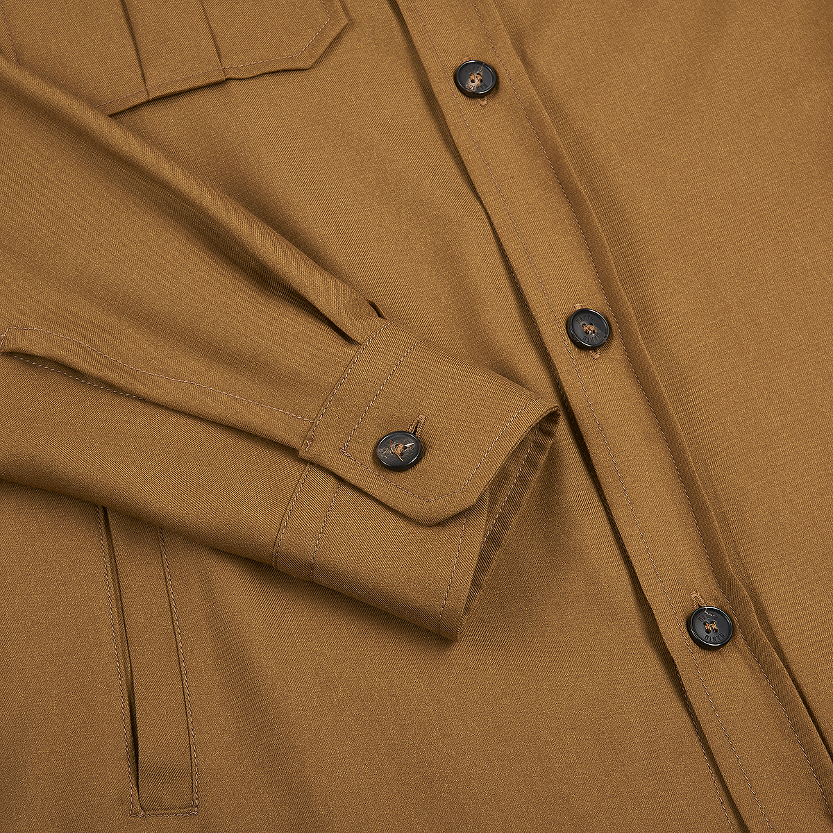 A close-up of the Camel Wool/Silk Gubbio Overshirt by Manto shows black buttons, a chest pocket with flap, visible seam, and cuff with buttoned sleeve folded over, highlighting its thick, smooth fabric for lasting durability. , available at Richard Gelding Mayfair