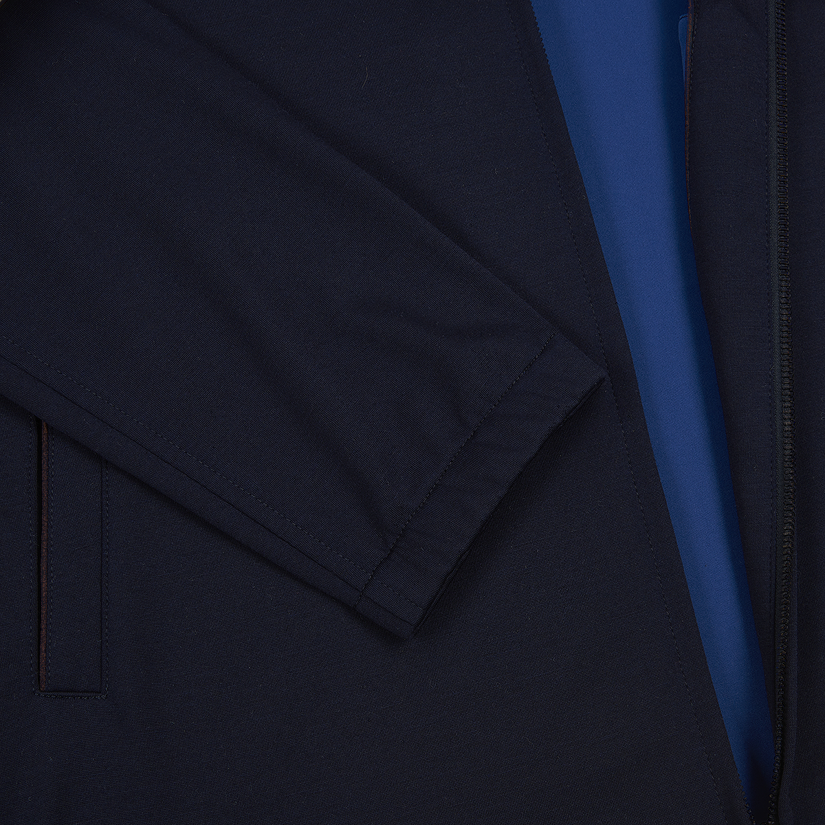 A close-up of the Manto Navy Loro Piana Wool/Silk Rain System Asiago Blouson highlights a folded sleeve, smooth fabric, and visible zipper, with a strip of bright blue fabric beneath the jacket opening. , available at Richard Gelding Mayfair