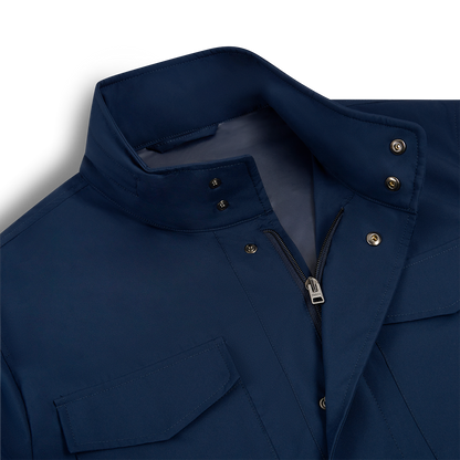 A close-up of the Manto Navy Japanese Nylon Andromeda Packable Field Jacket highlights Japanese precision in its standing collar with snap buttons, silver zipper, and flap chest pocket. The smooth, lightweight fabric stands out against a light background. , available at Richard Gelding Mayfair