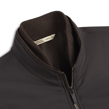 Close-up of the Maurizio Baldassari Chocolate Brown Nylon Gilet featuring a ribbed knit collar, smooth matte finish, and silver zipper. A beige “MADE IN ITALY” tag inside highlights the quality of this weather-resistant outerwear. , available at Richard Gelding Mayfair