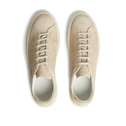 A pair of Beige Suede Leather Racquet sneakers with white laces, displayed from above on a striped background.