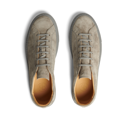 A pair of Granit Grey Suede Leather Racquet Sr sneakers by CQP with laces, viewed from above on a striped black and white background.