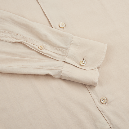 The image shows an Alessandro Gherardi Beige Muslin Beach Shirt laid flat with one sleeve folded across the body, cream-colored buttons, a single-button cuff, and detailed stitching on its smooth, slightly textured fabric. , available at Richard Gelding Mayfair