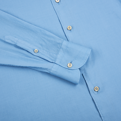 The Alessandro Gherardi Blue Muslin Cotton Blend Beach Shirt is shown lying flat with its left sleeve extended, highlighting the cuff, cream-colored buttons, and precise stitching on the smooth, neatly pressed fabric. , available at Richard Gelding Mayfair