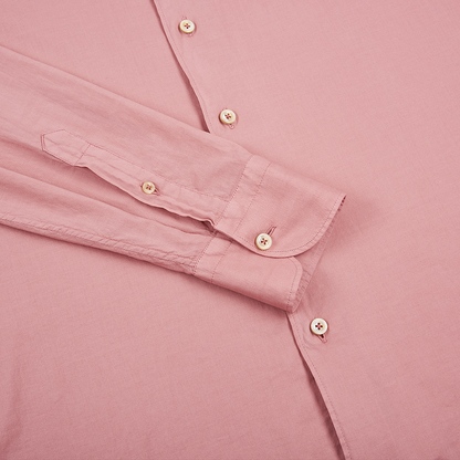 A close-up of the Alessandro Gherardi Pink Muslin Cotton Blend Beach Shirt shows its light pink hue, matching buttons, visible stitching on the placket and cuff, and one long sleeve neatly crossed over the shirt body. , available at Richard Gelding Mayfair
