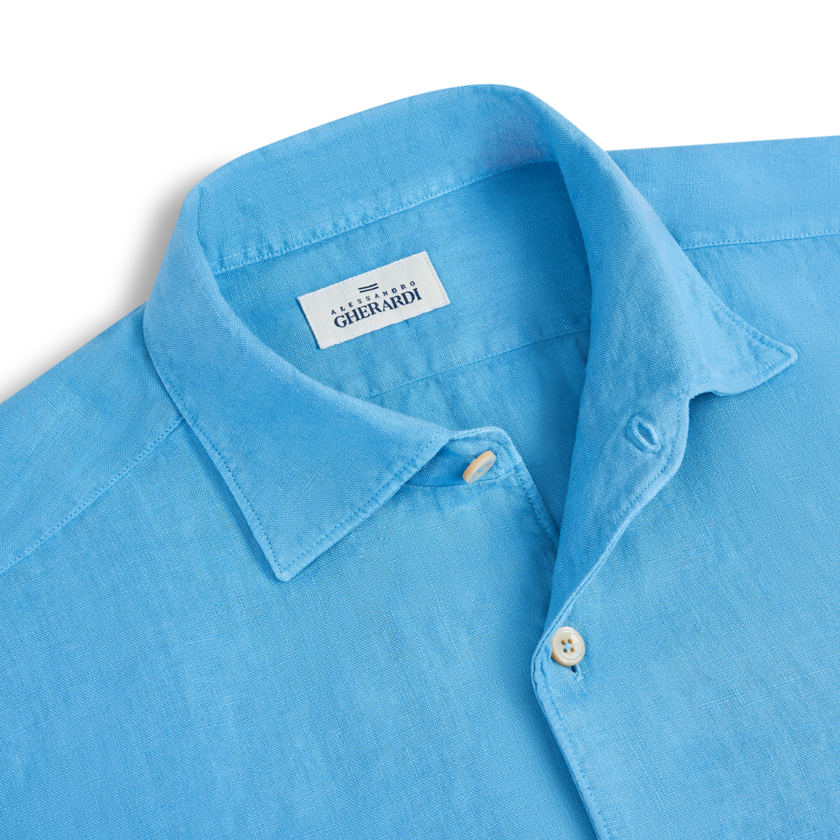 A close-up of the Alessandro Gherardi Mid Blue Linen One Piece Collar Casual Shirt, featuring a soft, textured fabric, cream buttons, and a brand label sewn inside the collar. The shirt is neatly laid flat. , available at Richard Gelding Mayfair