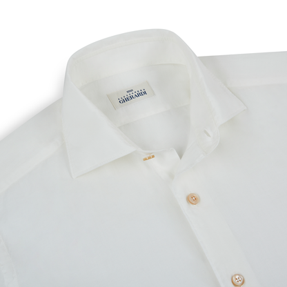 A close-up of a neatly folded Alessandro Gherardi White Muslin Beach Shirt shows its classic collar, light brown buttons, and inner label against a plain white background. , available at Richard Gelding Mayfair
