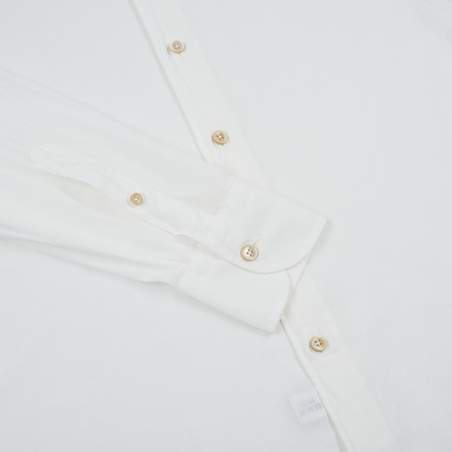 A close-up of the Alessandro Gherardi White Muslin Beach Shirt, neatly folded on a white surface. Cream-colored buttons, visible cuff and sleeve, part of the front placket, and a small white tag near the bottom edge are shown. , available at Richard Gelding Mayfair