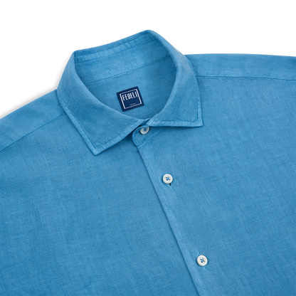 A close-up of the Fedeli Blue Linen Cutaway Collar Nick ML Shirt features white buttons and a visible Fedeli label inside the collar, laid flat on a white background. Made from lightweight linen with a stiff cutaway collar for a refined look. , available at Richard Gelding Mayfair