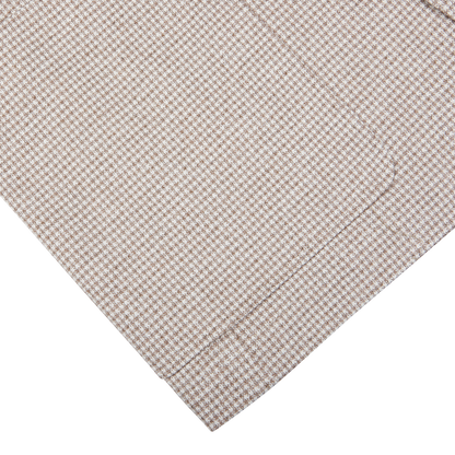 Close-up of a beige houndstooth Canali cotton jersey blazer fabric with a folded corner against a white background.