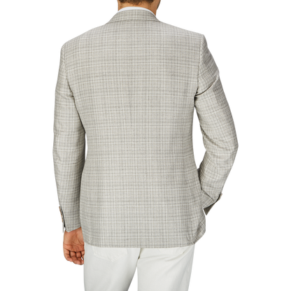 Rear view of a person wearing a Canali Beige Melange Silk Wool Basketweave Blazer with white trousers on a gray background.