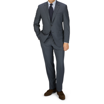 A man in a tailored Canali Grey-Blue Melange Wool Suit, white shirt, and blue tie stands with his left hand in his pocket, against a light gray background.