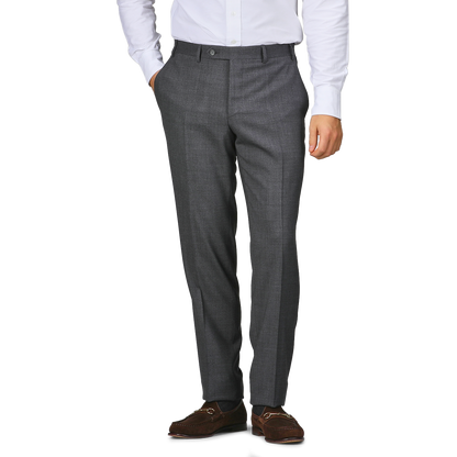 A person wearing Canali Grey Melange Wool Flat Front Trousers, a white shirt, and brown shoes stands with one hand in their pocket.