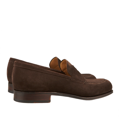 A pair of Carmina brown suede forest penny loafers on a striped background.