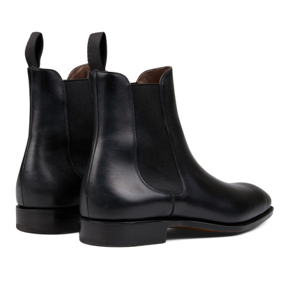 A pair of sleek black leather Simpson Chelsea boots with brown lining and pull tabs on a white background, crafted by expert craftsmen.