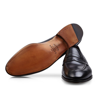 A single Carmina black calf leather Uetam penny loafer lying on its side with the sole facing up.