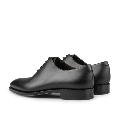 A pair of Black Calf Leather Wholecut Rain Oxford Shoes from Carmina is elegantly displayed at an angle, highlighting their polished finish and simple design. Featuring Goodyear welted construction, these timeless classics promise durability and style.