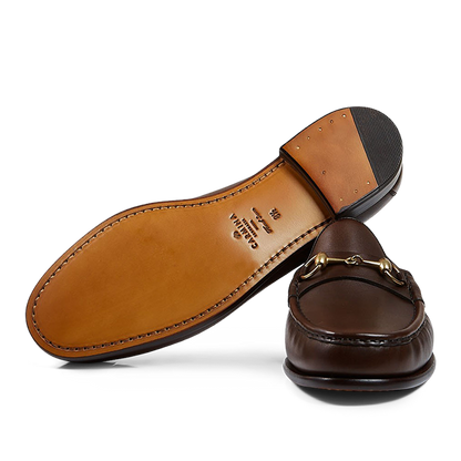 A pair of brown Carmina leather Xim horsebit loafers with gold-tone hardware, placed against a transparent background.