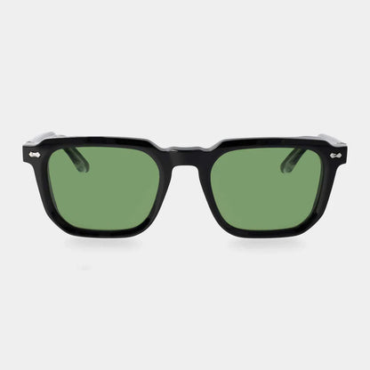 The Dart Black | Green sunglasses by TBD Eyewear feature thick, glossy black sustainable acetate frames and green mineral glass lenses. Handcrafted in Italy, they are shown front-facing on a light gray background with detailed silver hinges at the temples. , available at Richard Gelding Mayfair