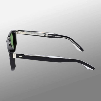 The Dart Black | Green sunglasses by TBD Eyewear feature thick black sustainable acetate frames, green mineral glass lenses, and textured silver details at the hinges, with handcrafted Italian quality shown against a gray gradient background. , available at Richard Gelding Mayfair