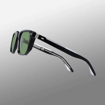 The Dart Black | Green sunglasses by TBD Eyewear feature sustainable black acetate frames, green-tinted rectangular lenses, and thick curved arms with metallic hinges, shown against a gradient grey background. , available at Richard Gelding Mayfair