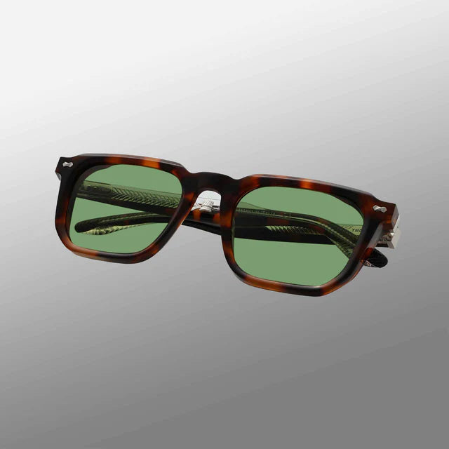 The Dart Brown Havana | Green sunglasses by TBD Eyewear are square with thick, recyclable brown havana acetate frames and green-tinted lenses. Displayed at an angle against a gray gradient background, the arms are partially folded. , available at Richard Gelding Mayfair