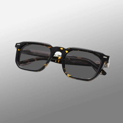 The Dart Eco Black Havana | Grey by TBD Eyewear features rectangular black havana frames in thick, dark tortoiseshell acetate with yellow and amber flecks, grey lenses offering 100% UV protection, and a minimalistic modern design. , available at Richard Gelding Mayfair