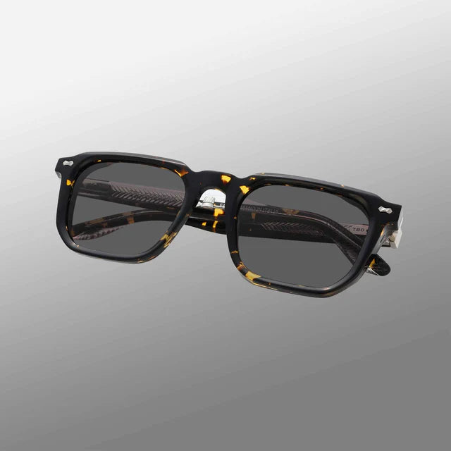 The Dart Eco Black Havana | Grey by TBD Eyewear features rectangular black havana frames in thick, dark tortoiseshell acetate with yellow and amber flecks, grey lenses offering 100% UV protection, and a minimalistic modern design. , available at Richard Gelding Mayfair