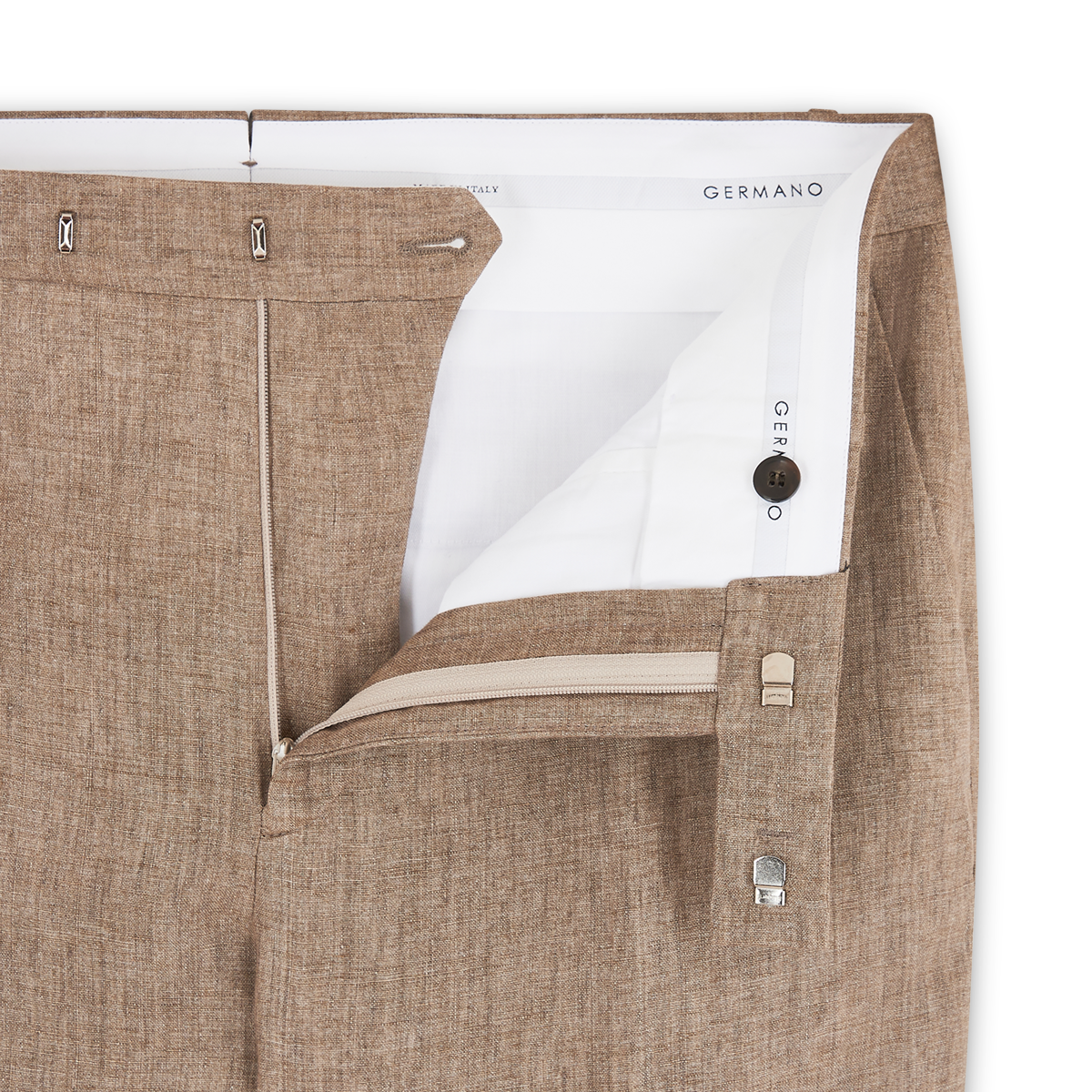 A close-up of light brown linen formal trousers by Germano shows the open waistband and fly, revealing a white inner lining, zipper, button, metal clasp, and part of the Germano label inside. , available at Richard Gelding Mayfair