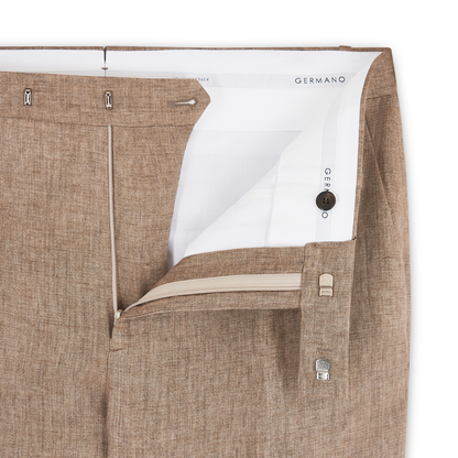 A close-up of light brown linen formal trousers by Germano shows the open waistband and fly, revealing a white inner lining, zipper, button, metal clasp, and part of the Germano label inside. , available at Richard Gelding Mayfair